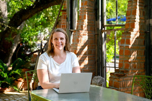Founder of Hem sitting outdoors with a laptop, smiling while working on pelvic health support tools.